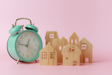 A bell alarm clock with wooden house model on pink background for the concept of time management, housing and property.の写真素材