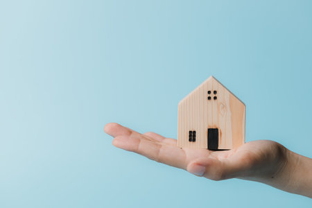 Hand holding a wooden house model on blue background for housing and property conceptの写真素材