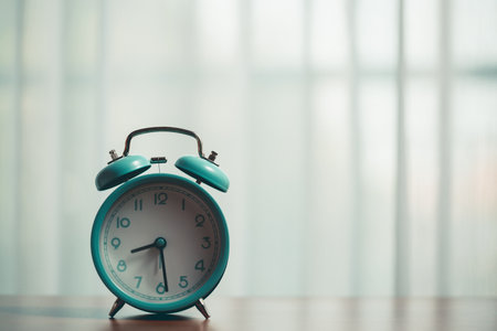 Table with a vintage alarm clock, set against the curtains with morning sunlight shining on,...