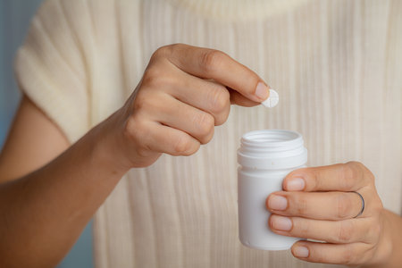 Closeup of woman hand holding white plastic bottle with pills for medical and healthcare concept, Focus on foreground.の写真素材