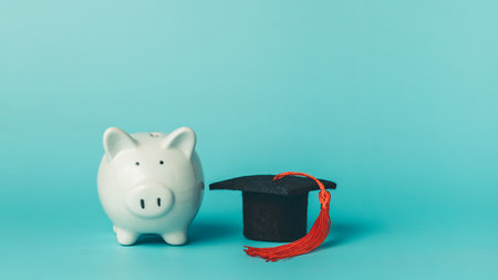 Piggy bank with graduation cap on blue background. Symbol of saving money, student loans, tuition fees, and financial planning for education.の写真素材
