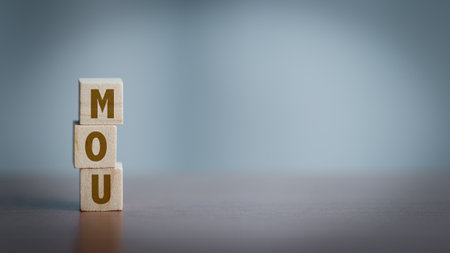 Wooden cubes with the word MOU on wooden table. Concept of business agreement, memorandum of understanding, partnership, negotiation, and corporate collaboration.の写真素材