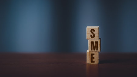 Stacked wooden cubes spelling SME on dark toned table with blurred background. Concept of small business, entrepreneurship, startup, finance, and economic growth.の写真素材
