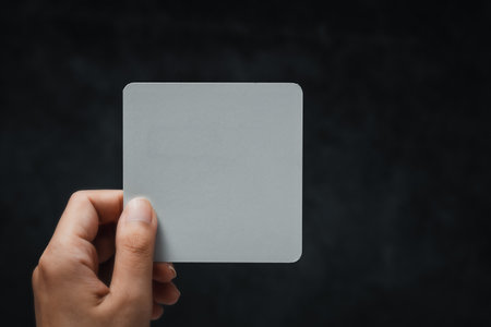 Woman's hand holding white note against black background. Concept of message, communication, minimal design, announcement, and copy space for text or branding.の写真素材