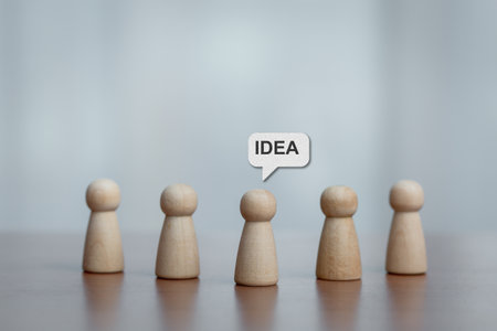 Five wooden figurines standing together, center figure with 'IDEA' speech bubble. Concept of brainstorming, teamwork, leadership, creativity, and innovation.の写真素材