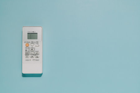 A white air conditioner remote control with digital display on light blue background with space for...