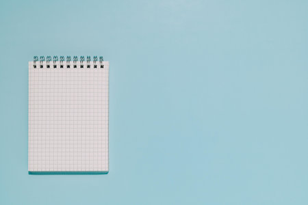 An open, blank grid notepad on a clean, light blue background. Perfect for themes of planning,...