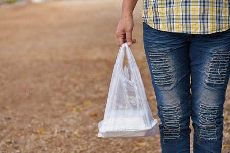 lady in fashionable ripped jeans stands in light green wall. woman taking a plastic bag of packed...