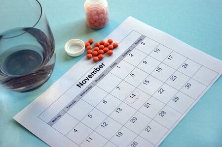 Inverted jar with orange pills and a calendar with marked dates on a blue backgroundの写真素材