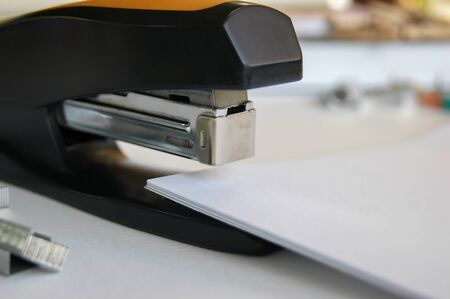 Classic black office stapler with documents. In the work field.