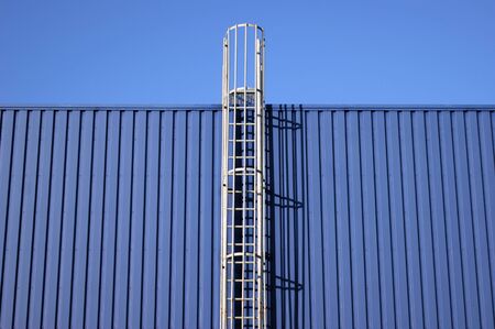 Blue background metal wall siding, cladding with stairs to the roof. Reflective metallic convex...