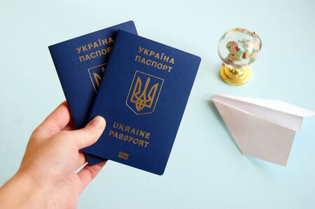 Two Ukrainian biometric passports in the hands of a woman on a light blue background with a globe and a paper plane.の写真素材