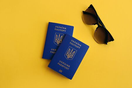 Two Ukrainian biometric passports with women's glasses on a yellow background. Travel conceptの写真素材