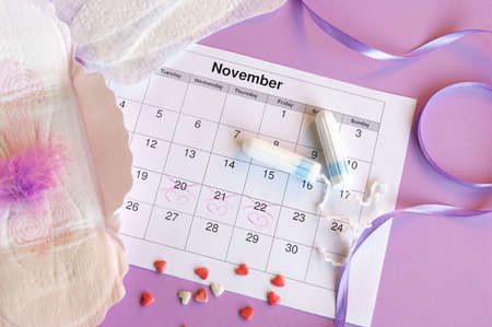 Menstrual pads and tampons on menstruation period calendar with on lilac background.の写真素材