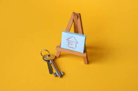 Drawing of a house on a wooden easel, nearby are the keys on a yellow background. The concept of...