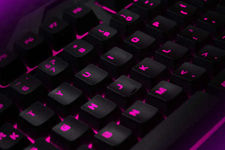 Backlit gaming keyboard close up. Black keys with pink illuminated characters.