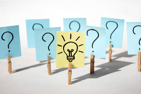 A lot of clothespins with question marks on stickers and on one light bulb, as a sign of a good idea. Concept of business, management, markets, creativity.の写真素材