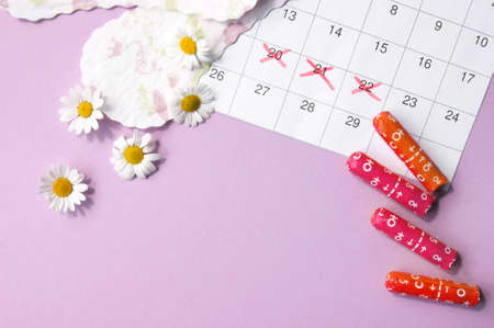 Menstrual pads and tampons on menstruation period calendar with chamomiles on pink background. The...
