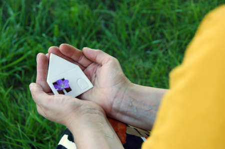 Hands holding white paper house, family home, homeless housing and home protecting insurance concept, international day of families, foster home care, family day care, social distancing.の写真素材