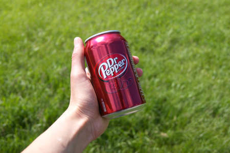 KHARKOV, UKRAINE - JUNE 12, 2020: Hand holds metal can of Dr. Pepper on a background of green grass.