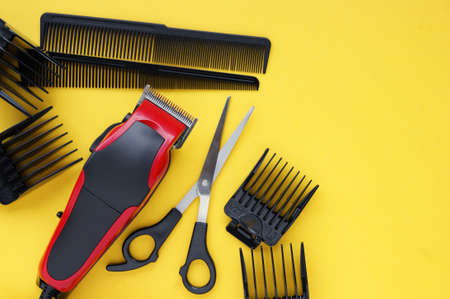 Hairdressers tool. Hair clipper close-up on a yellow background with nozzles of different sizes, scissors and combs.の写真素材