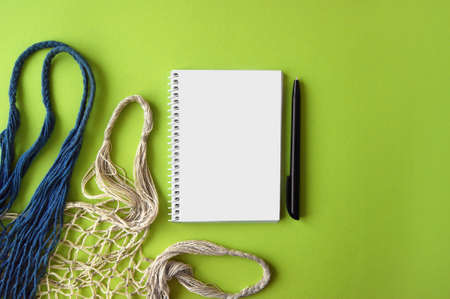Two reusable shopping bag and notebook with pen on green background. Ecological concept. Top view of mesh cotton shopping bag. Caring for the environment and the rejection of plastic.の写真素材