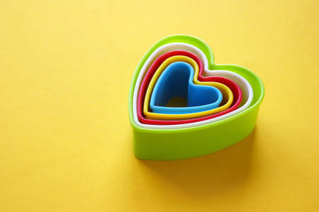 Plastic molds of multi colors for making cookies in the shape of a hearts on a yellow background. Culinary or party concept. Copy space.の写真素材