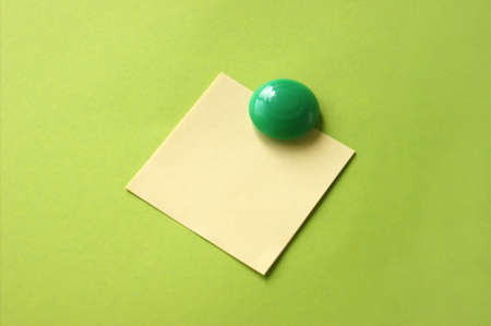 Yellow sticker with blank space for inscription or reminder on a green background, attached to a...
