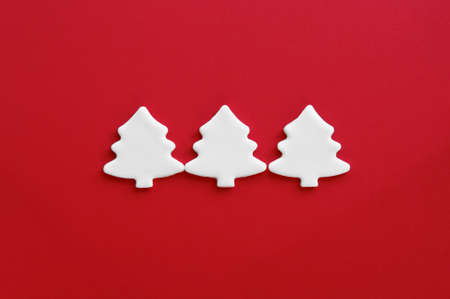 White carved christmas trees of mastic on red background. Winter holiday. Christmas pattern with snow effect. Modern, minimalist and uncluttered mockup with copy space.の写真素材