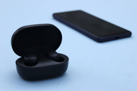 Smartphone and wireless  headphones or earbuds with charging case on bright blue background. Music technology trends 2020-2021.の写真素材