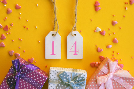 Date 14 on a wooden tag with gifts and hearts for Valentines Day. Yellow backgroundの写真素材