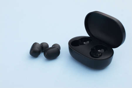 Wireless headphones or earbuds with charging case on bright blue background.