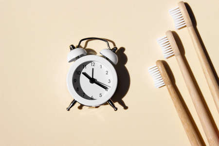 Bamboo toothbrushes, and small white alarm clock on light background. Say no to plastic concept. Top...