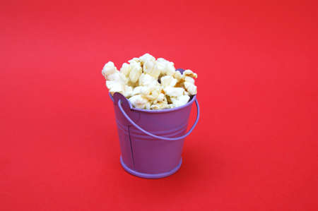 Fresh popcorn in a small decorative iron bucket on a red background.の写真素材