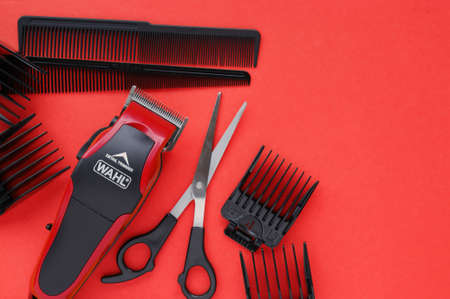 Hair clipper WAHL close-up on a red background with nozzles of different sizes, scissors and combs.のeditorial素材