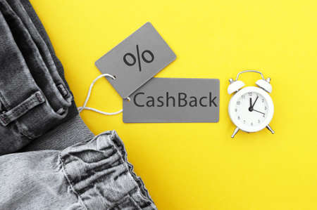 Flat lay, detail of black jeans, gray labels and inscription CashBack on yellow background. Shopping...