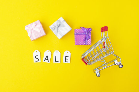 Shopping cart with gifts and white labels with the word SALE on a yellow background. Shopping and discount concept. Black Friday.の写真素材