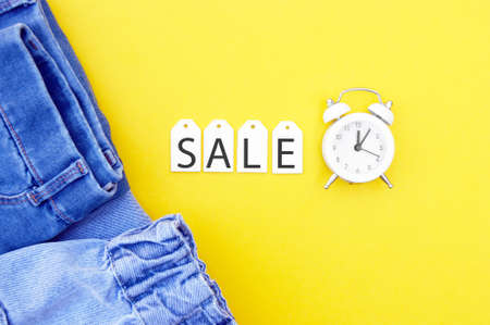 Flat lay, detail of jeans, white labels and inscription Sale on yellow background. Shopping and discount concept. Black Friday.の写真素材