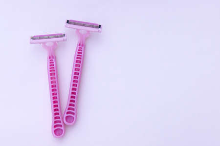 Man and woman body treatment of depilation with razor and skin care concept. Closeup view with selective focus of pink disposable shaver on pink background.の写真素材