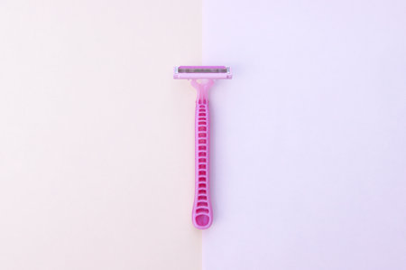 Man and woman body treatment of depilation with razor and skin care concept. Closeup view with selective focus of pink disposable shaver on pink background.の写真素材