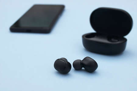 Smartphone and wireless headphones or earbuds with charging case on bright blue background. Music technology trends 2020-2021.の写真素材