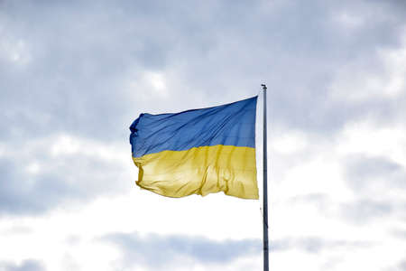 Large national flag of Ukraine flies in the blue sky. Big yellow blue Ukrainian state banner in the...