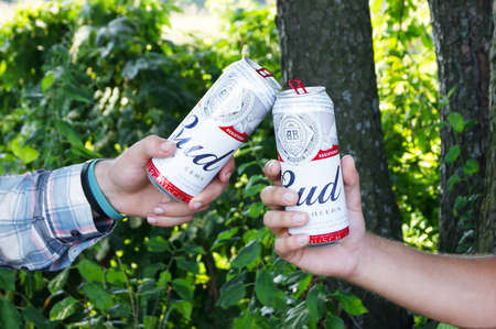 KHARKIV, UKRAINE - AUGUST 1, 2021: Two guys are holding cans of Budweiser Lager Alcohol beer in nature. Budweiser is America's most popular Anheuser-Busch Inbev brand.のeditorial素材