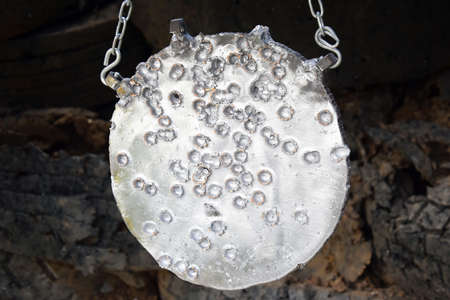 A metal target or gong for shooting sports firearms. Many holes from the shots.の写真素材