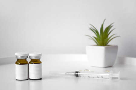 Cosmetic bottle for injection on the background of a syringe and a green flower. The concept of beauty treatments or vaccinations against virus and other diseases.の写真素材