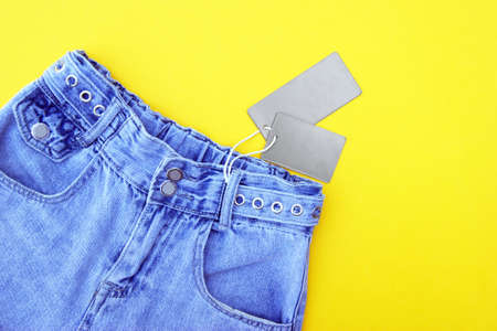 Flat lay, detail of denim jeans with blank gray label on yellow background. Shopping and discount...