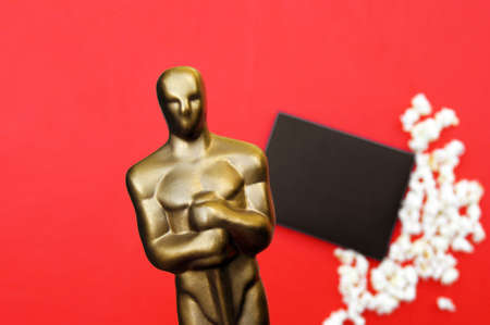 Plastic Oscar award on a red background with popcorn and a black envelope.