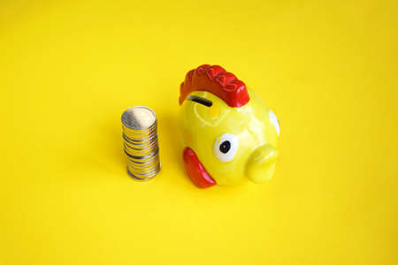 Yellow piggy bank in the form of a fish with coins stacked in a column. Savings concept.の写真素材