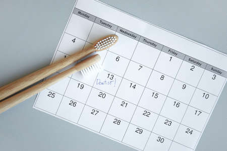On a light gray background, there is a calendar with a dentist's note and toothbrushes. Dental health concept.の写真素材