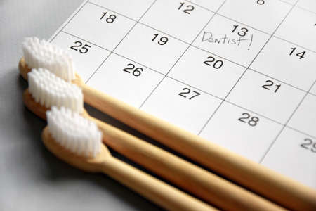 On a light gray background, there is a calendar with a dentist's note and toothbrushes. Dental...